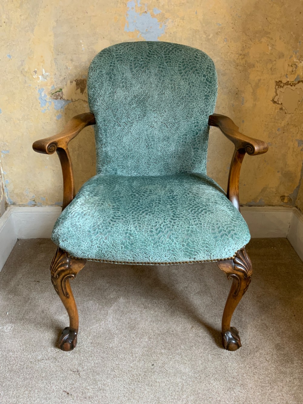 An antique walnut open armchair featuring light green textured upholstery, carved cabriole legs with ball and claw feet, and curved wooden armrests.