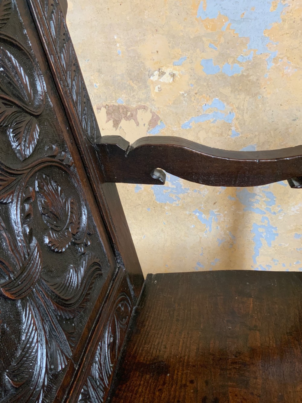 A dark oak 17th-century wainscot armchair featuring a high carved back panel with botanical motifs, turned front legs, and turned crest finials. View V