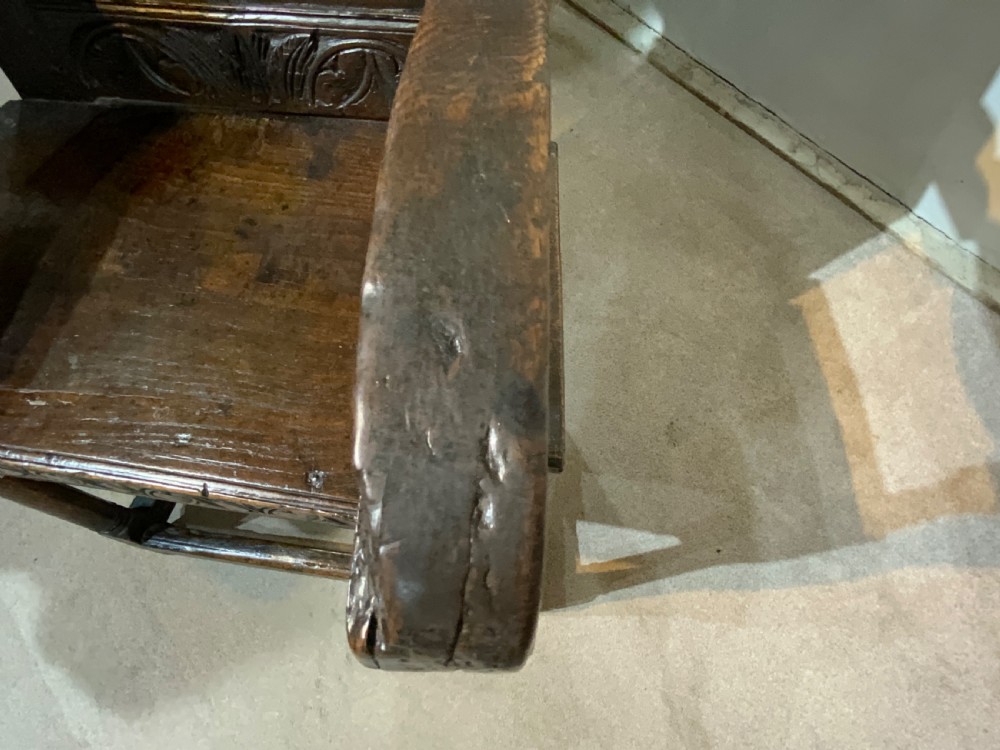 A dark oak 17th-century wainscot armchair featuring a high carved back panel with botanical motifs, turned front legs, and turned crest finials. View VIII