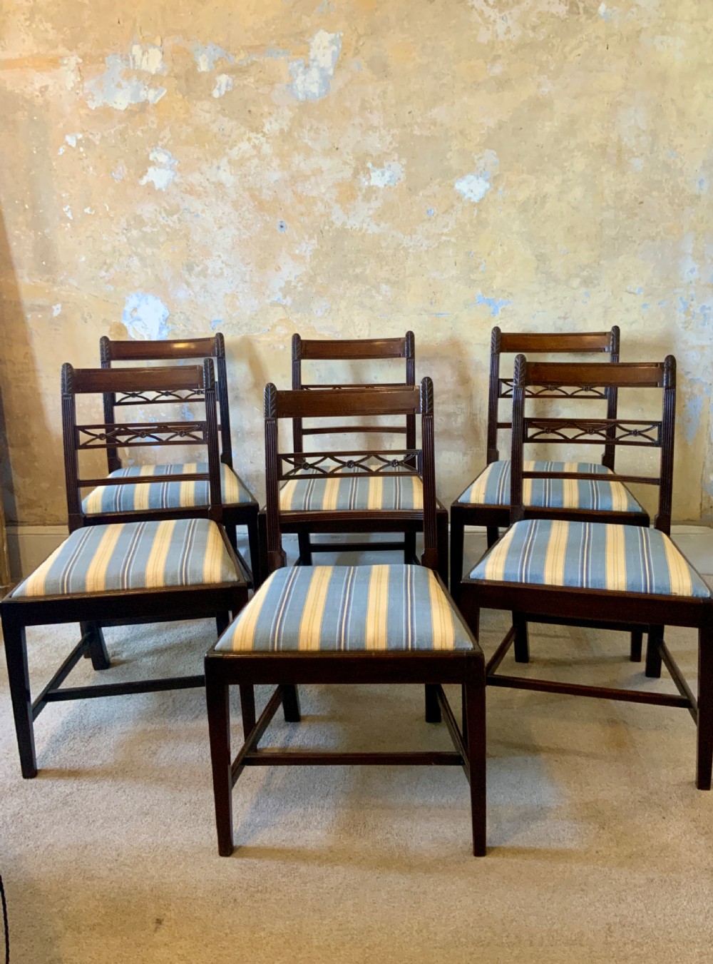 A set of six dark brown mahogany dining chairs featuring open ladder-backs with carved detailing and blue-and-yellow striped upholstered drop-in seats.