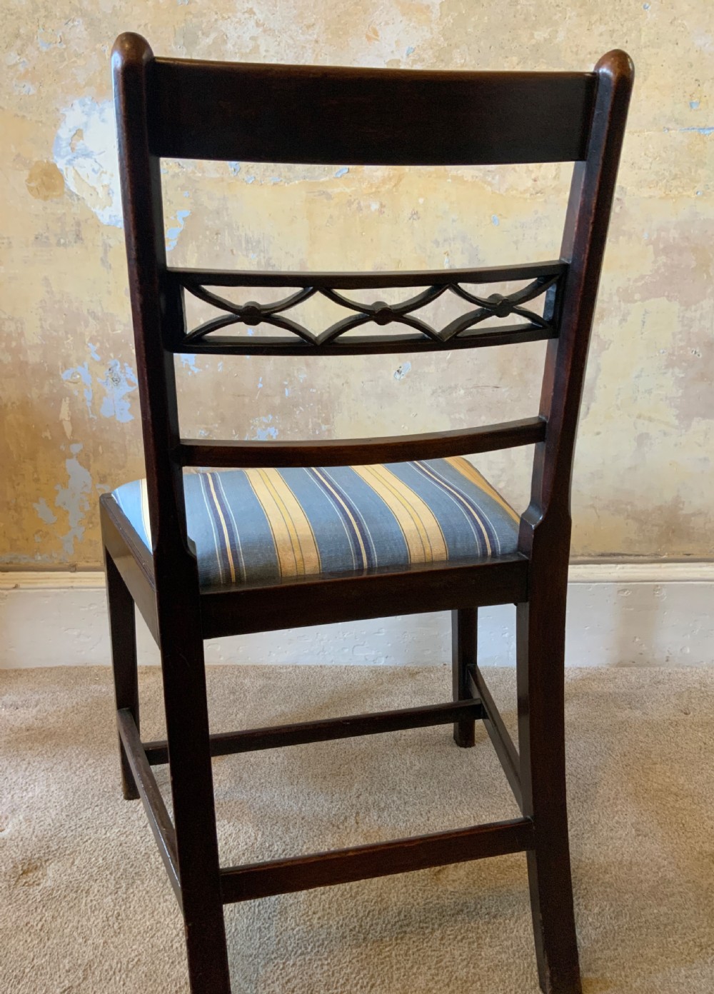 A set of six dark brown mahogany dining chairs featuring open ladder-backs with carved detailing and blue-and-yellow striped upholstered drop-in seats. View V