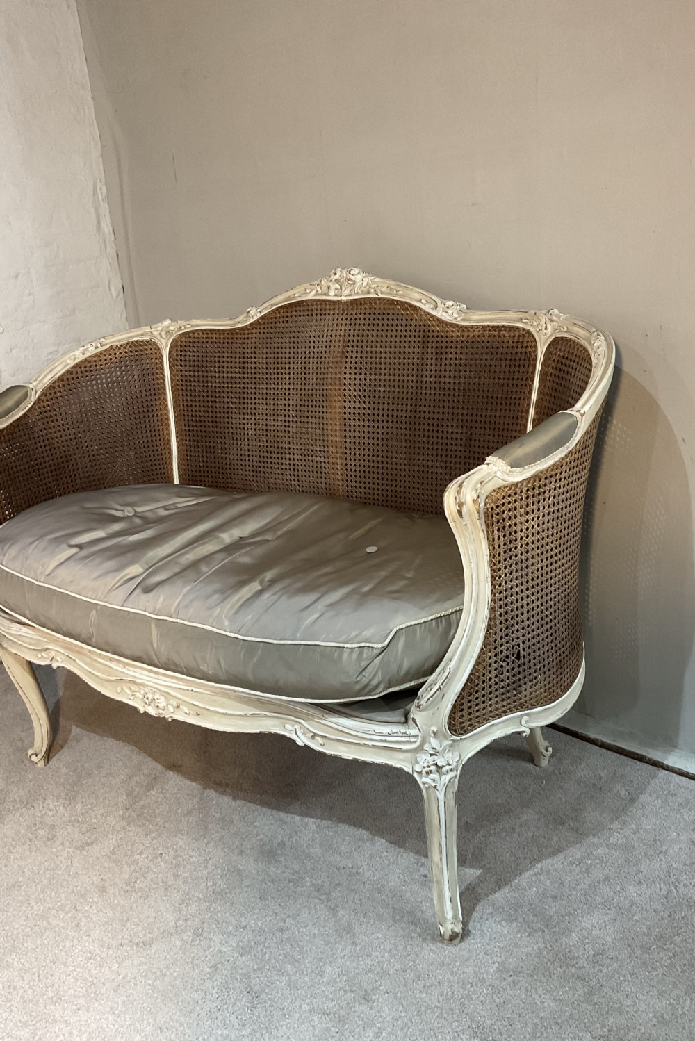 A 19th-century French bergere settee featuring a painted carved wooden frame with woven cane back panels and a champagne-coloured upholstered seat cushion with two accent pillows. View II