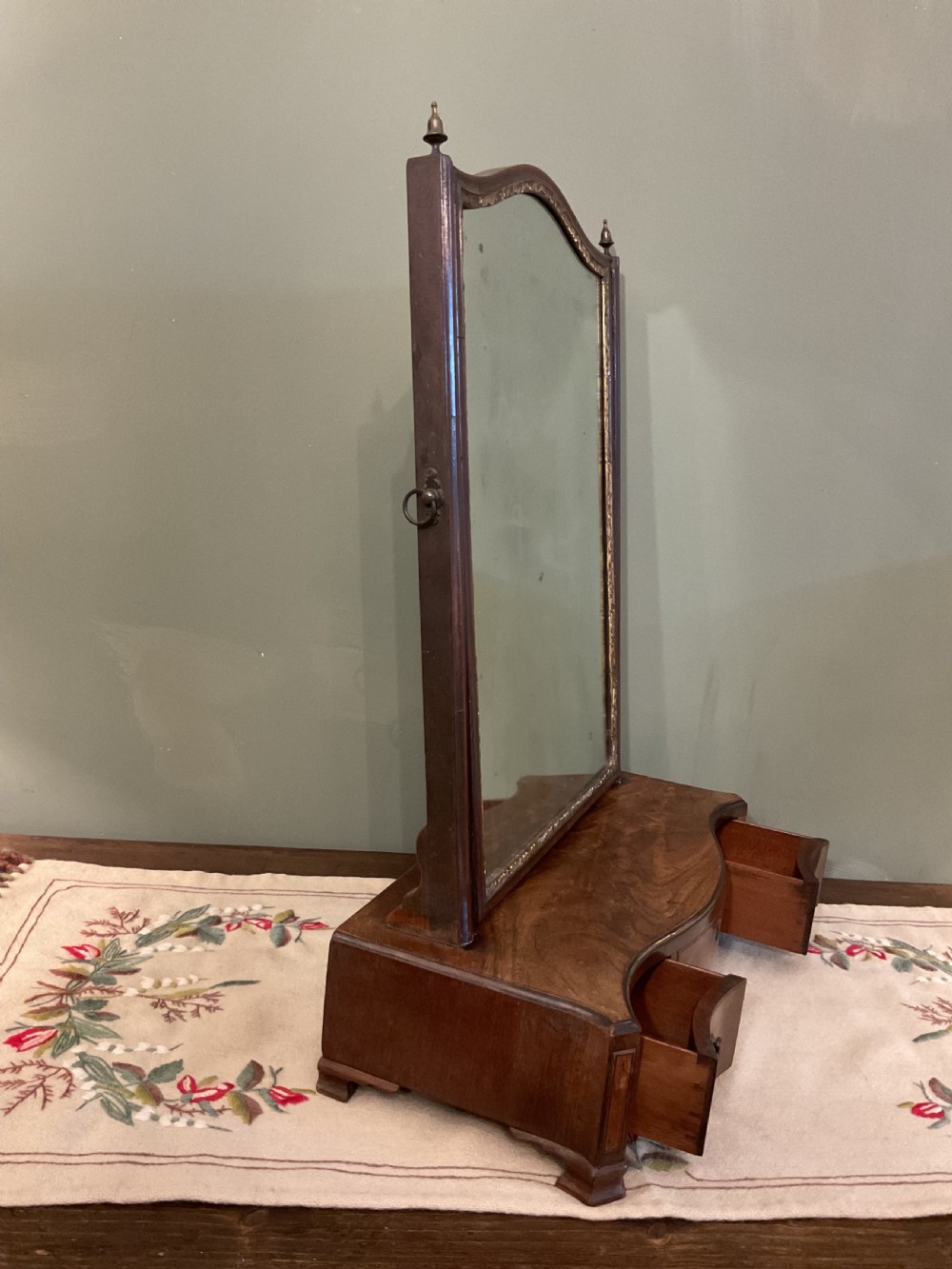 A George II period dark walnut toilet mirror featuring an arched adjustable swing frame set above a shaped three-drawer base with brass handles. View III