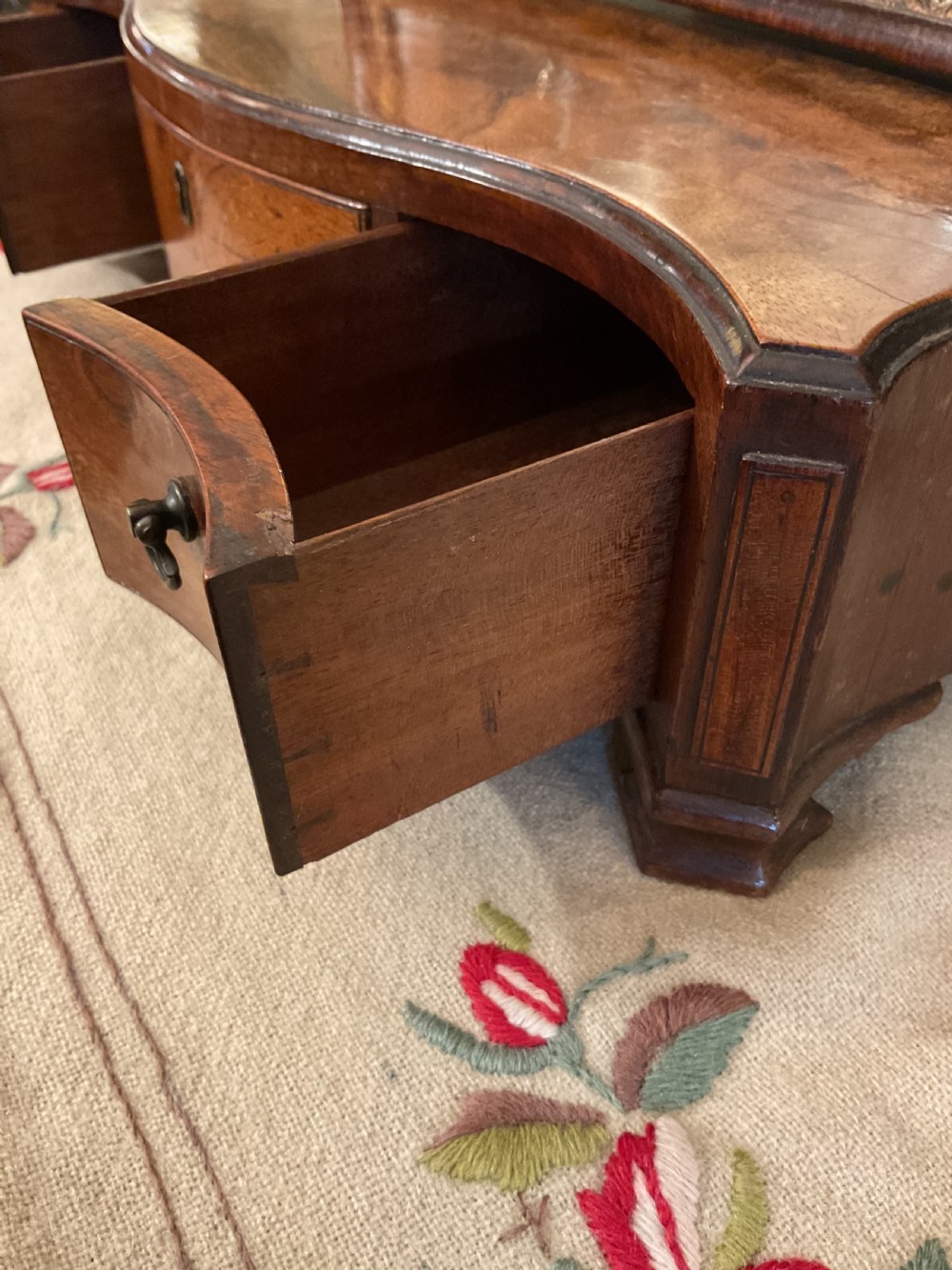 A George II period dark walnut toilet mirror featuring an arched adjustable swing frame set above a shaped three-drawer base with brass handles. View VI