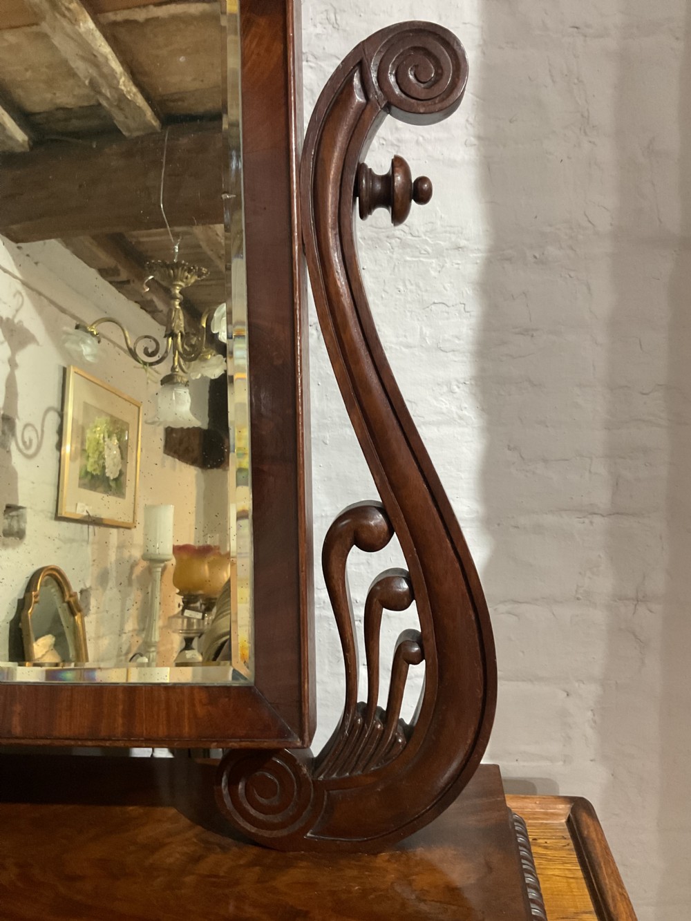 A Regency mahogany toilet mirror featuring a rectangular glass plate suspended between two carved scroll supports above a moulded plinth base. View II