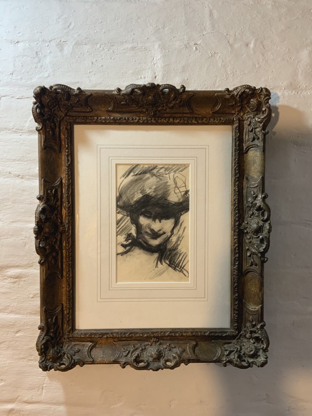 A framed charcoal portrait drawing of a woman wearing a hat, mounted inside an ornate carved gilt frame.