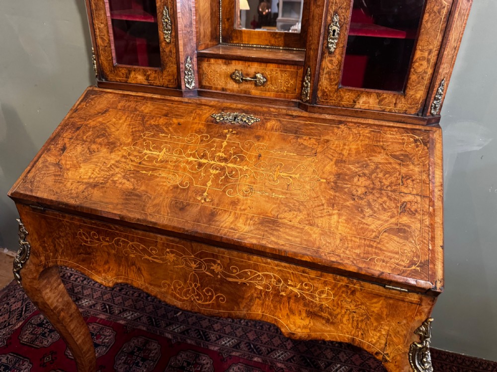 A burr walnut bonheur du jour writing desk featuring floral marquetry, cabriole legs with gilt bronze mounts, and an upper section with twin glazed cabinets framing a central mirror. View IV