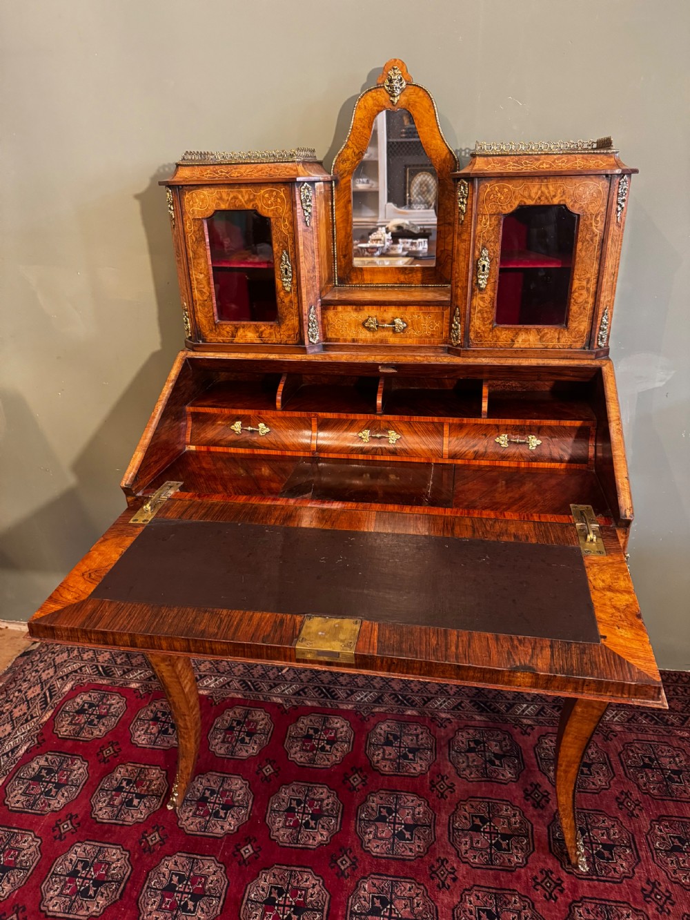 A burr walnut bonheur du jour writing desk featuring floral marquetry, cabriole legs with gilt bronze mounts, and an upper section with twin glazed cabinets framing a central mirror. View V