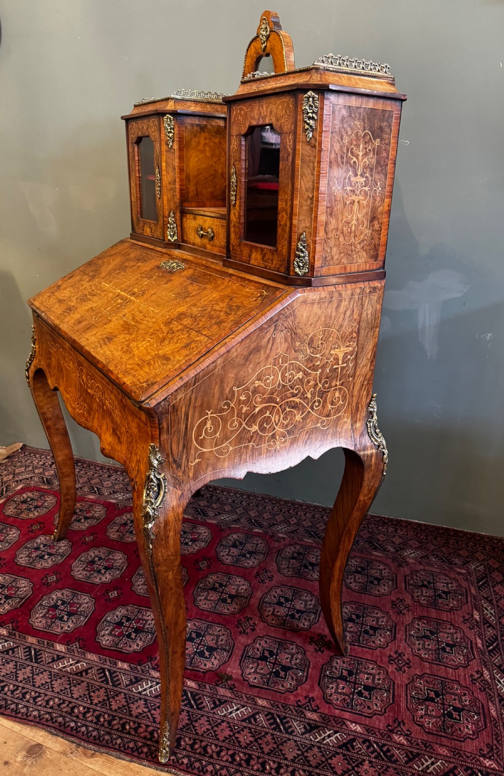 A burr walnut bonheur du jour writing desk featuring floral marquetry, cabriole legs with gilt bronze mounts, and an upper section with twin glazed cabinets framing a central mirror. View VII