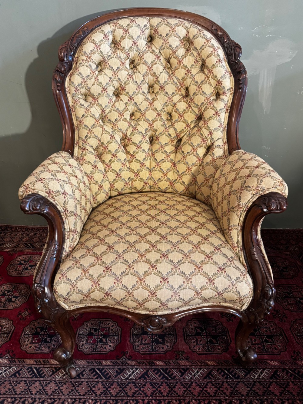 A Victorian mahogany armchair with patterned button-backed upholstery, carved wooden frame, and front cabriole legs.