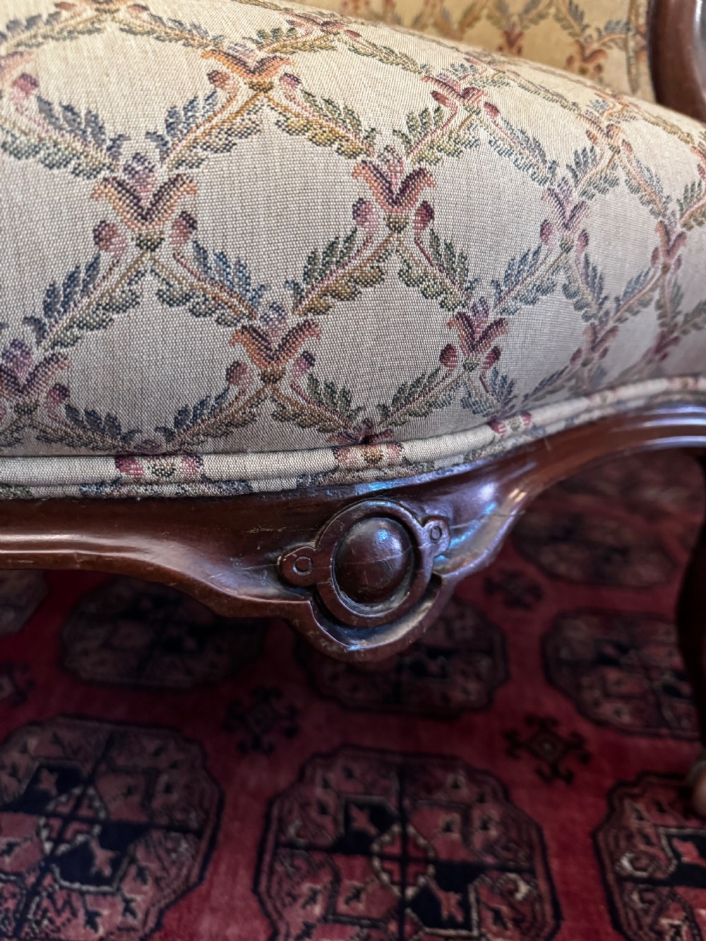 A Victorian mahogany armchair with patterned button-backed upholstery, carved wooden frame, and front cabriole legs. View V