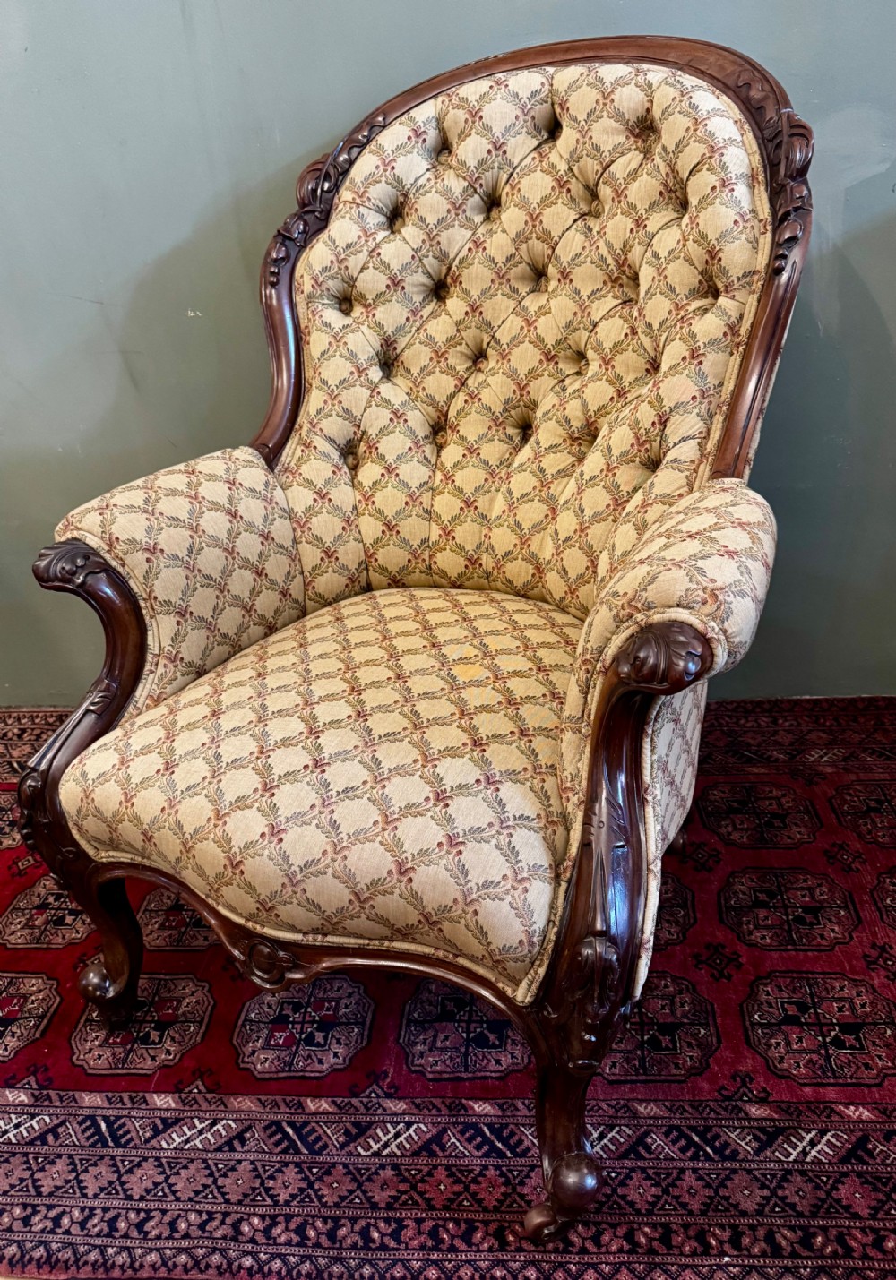 A Victorian mahogany armchair with patterned button-backed upholstery, carved wooden frame, and front cabriole legs. View X