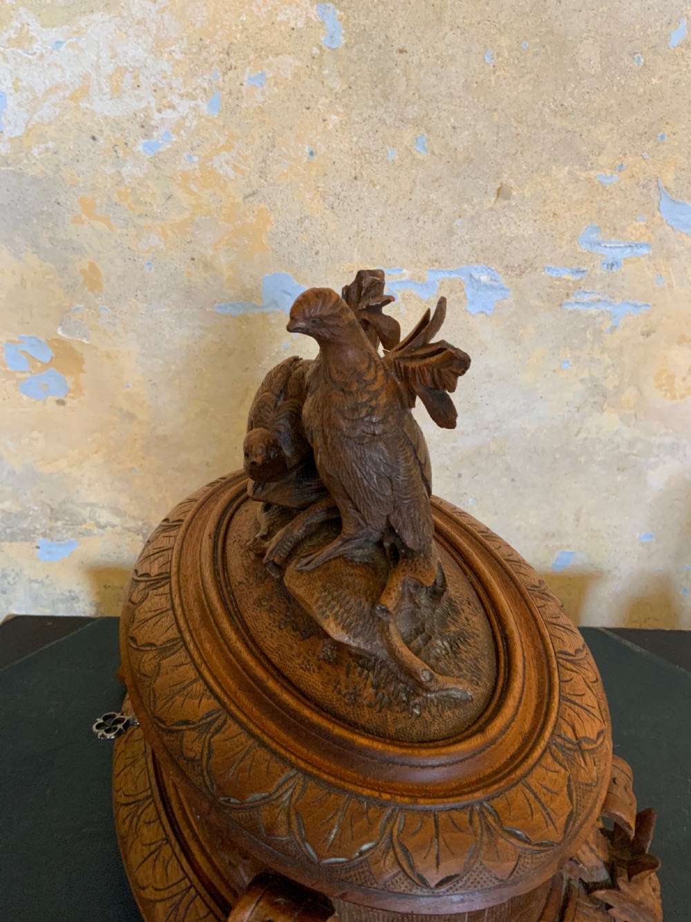 An antique carved wooden casket featuring a detailed top finial with two sculpted birds perched on foliage, sitting on carved feet with a keyhole in the front base. View IV