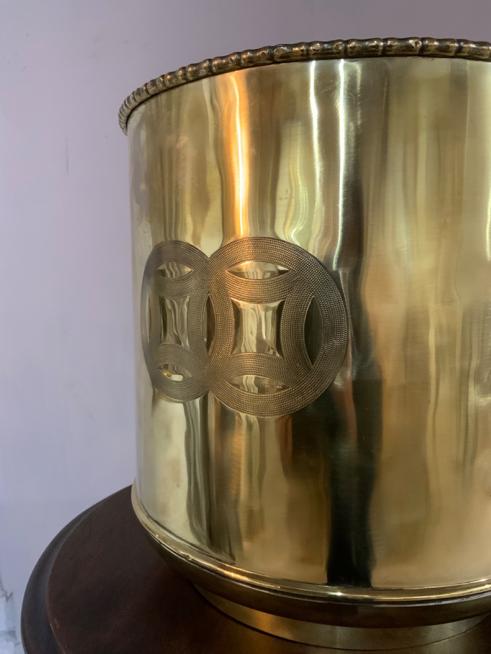 A pair of cylindrical polished brass planters featuring beaded rims, drop ring handles, and etched interlocking circle motifs. View VI
