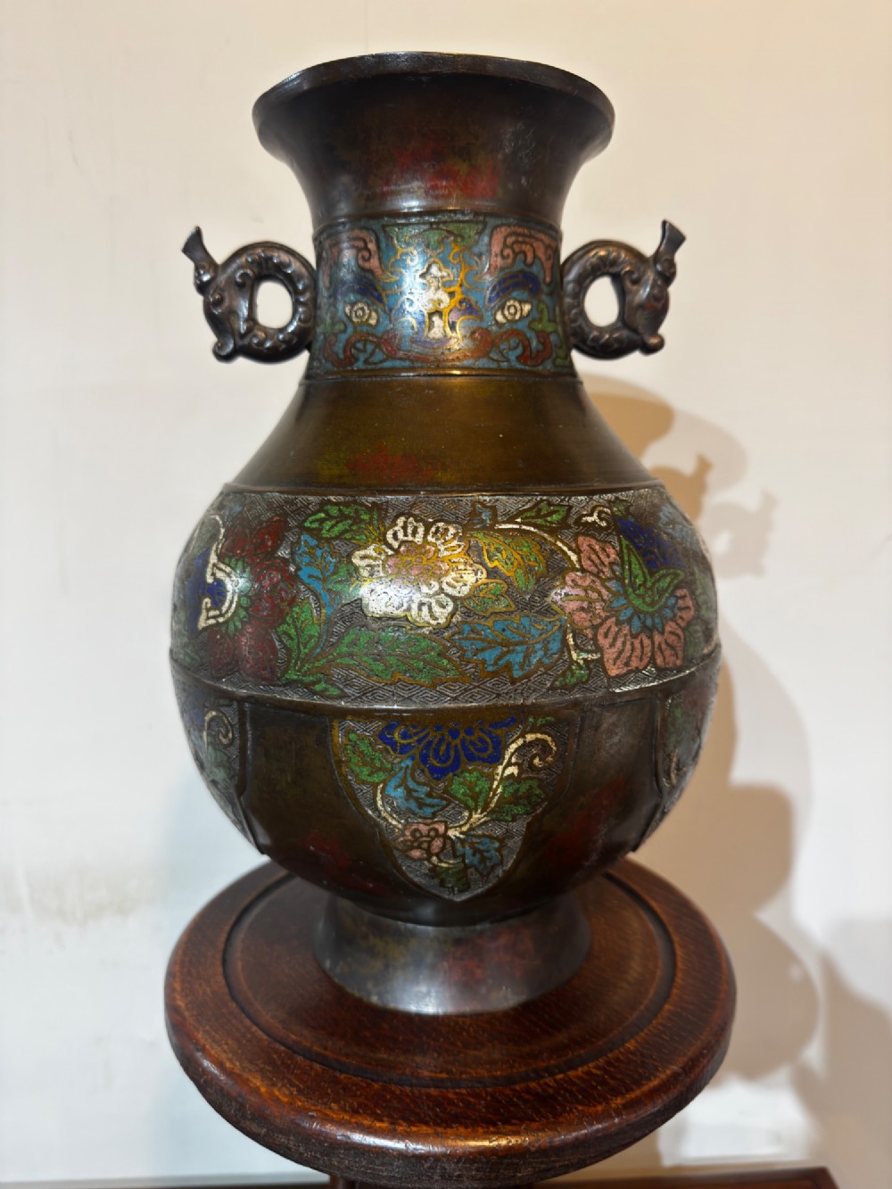 A dark patinated bronze vase with twin dragon handles and polychrome floral champleve enamelling around the body and neck.