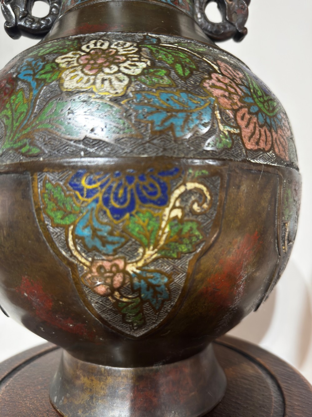 A dark patinated bronze vase with twin dragon handles and polychrome floral champleve enamelling around the body and neck. View II