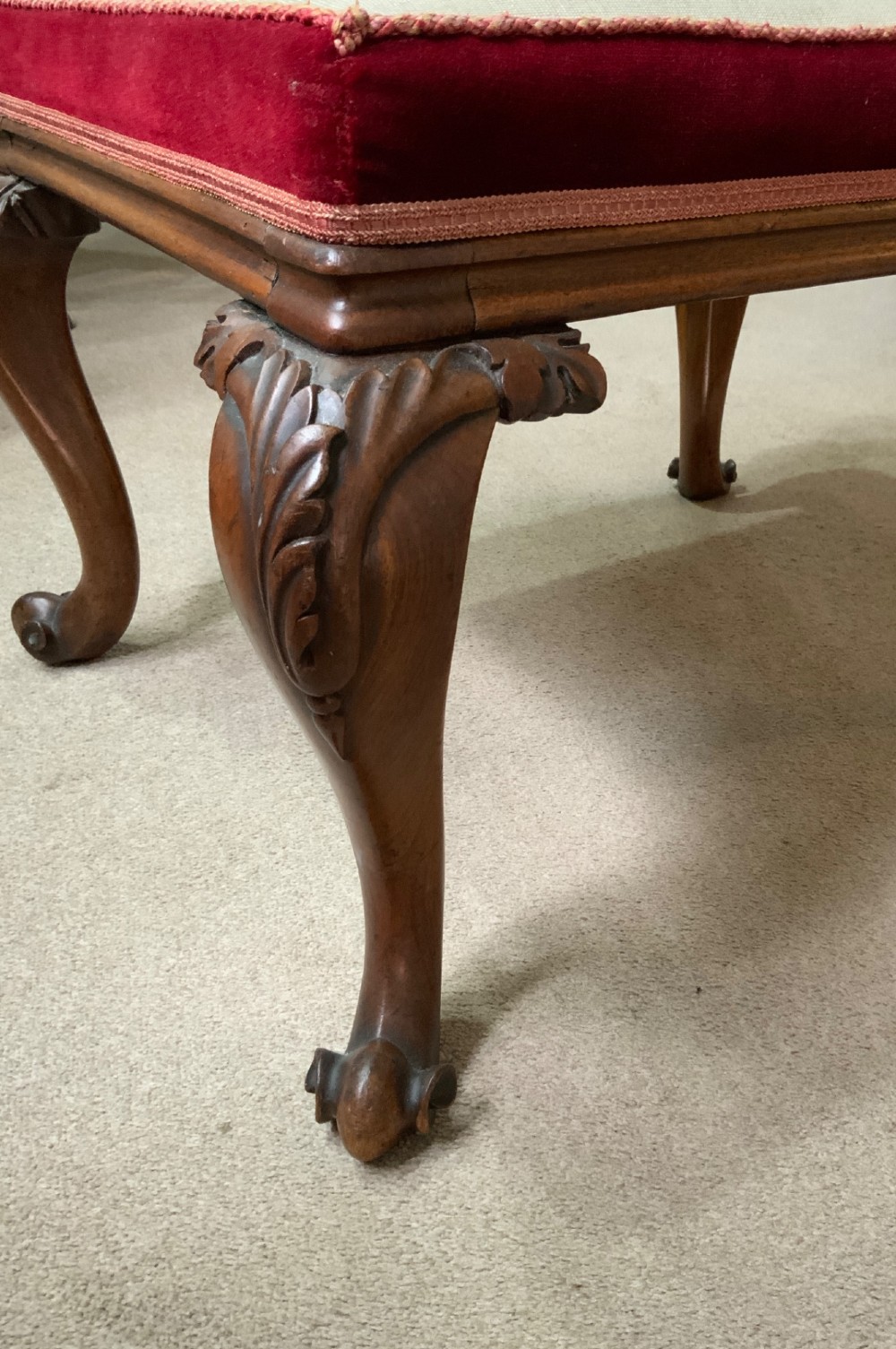 An antique mahogany footstool featuring carved cabriole legs and a floral needlepoint cushion bordered with burgundy velvet. View II