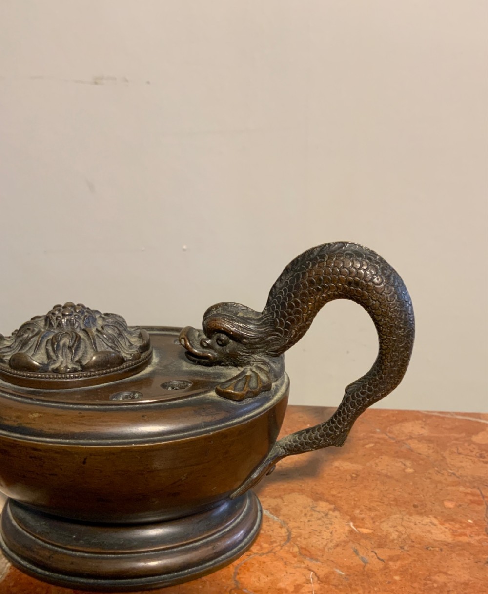 A dark patinated bronze inkwell styled as a classical Roman oil lamp featuring a sculpted serpent handle and a decorated lid. View II