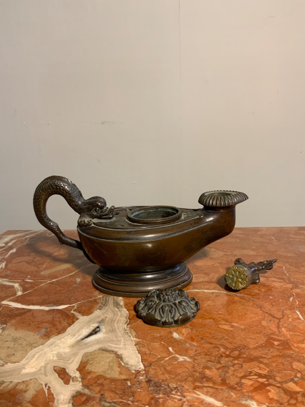 A dark patinated bronze inkwell styled as a classical Roman oil lamp featuring a sculpted serpent handle and a decorated lid. View V