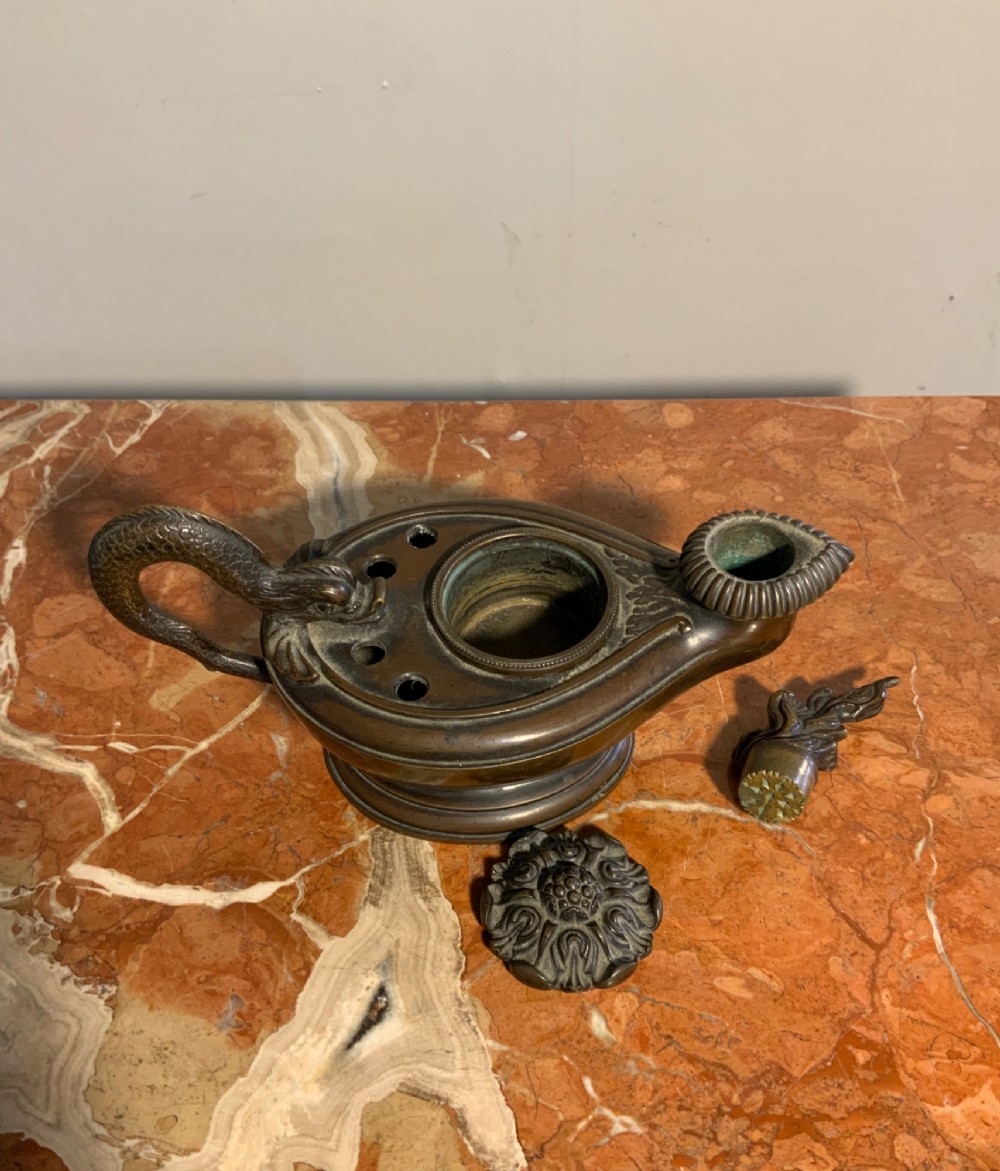 A dark patinated bronze inkwell styled as a classical Roman oil lamp featuring a sculpted serpent handle and a decorated lid. View VI