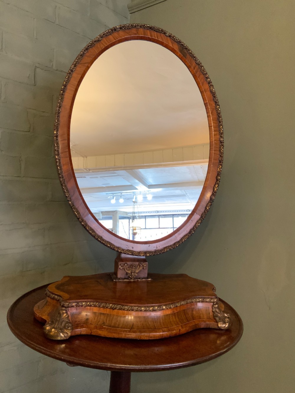 An oval walnut toilet mirror with an ormolu beaded border resting on a shaped serpentine base.