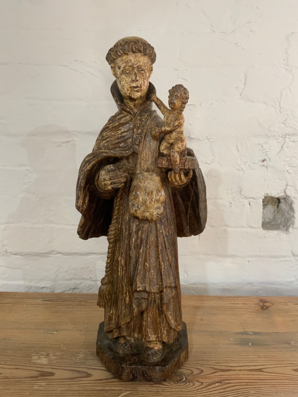 A carved wood figure representing Saint Anthony of Padua in a Franciscan habit holding the Christ Child on a open book.