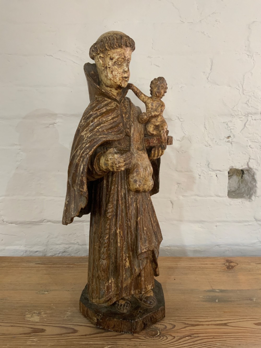 A carved wood figure representing Saint Anthony of Padua in a Franciscan habit holding the Christ Child on a open book. View II