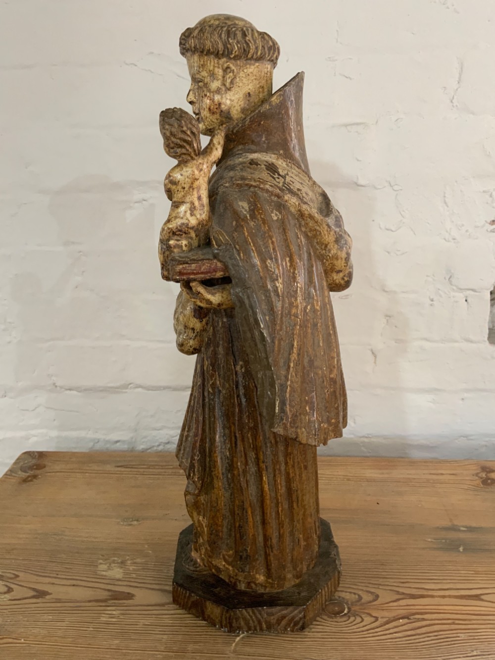A carved wood figure representing Saint Anthony of Padua in a Franciscan habit holding the Christ Child on a open book. View IV