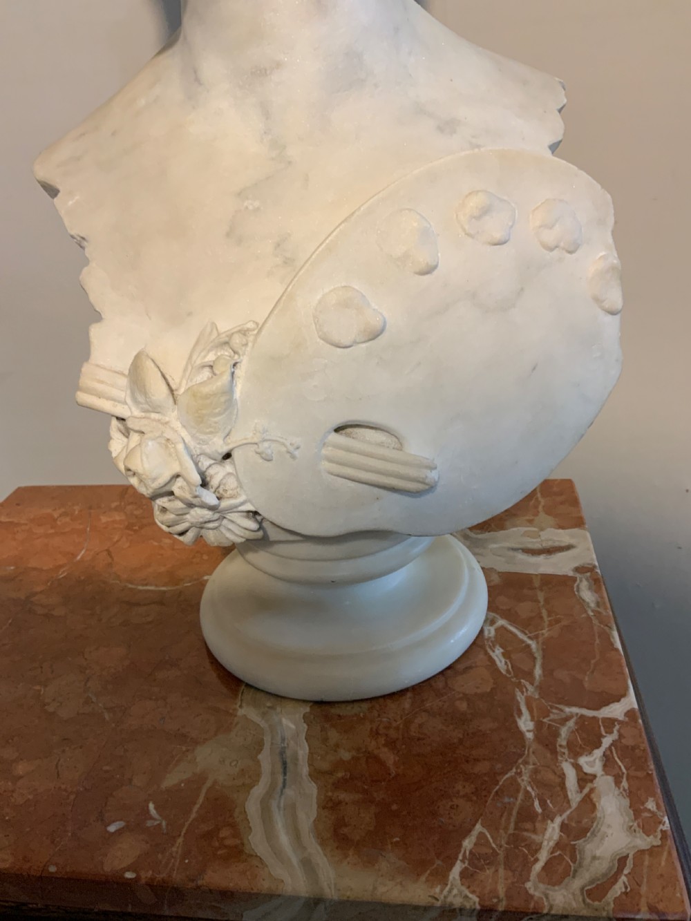 A carved white Carrara marble bust of a female figure featuring an artist palette and carved floral details, mounted on a turned socle. View VI