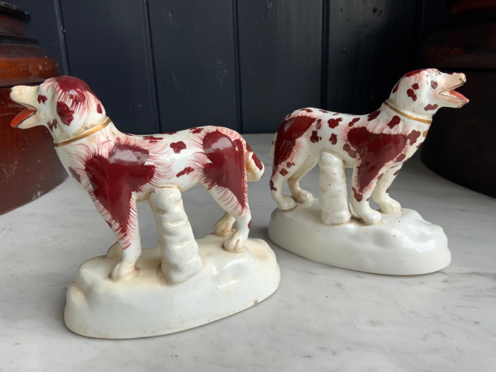 A facing pair of antique ceramic dog figurines decorated with rust-red painted patches on white bases with gilded collars. View II