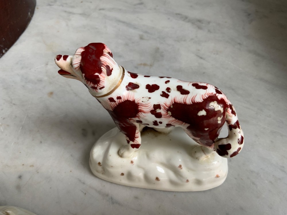 A facing pair of antique ceramic dog figurines decorated with rust-red painted patches on white bases with gilded collars. View V
