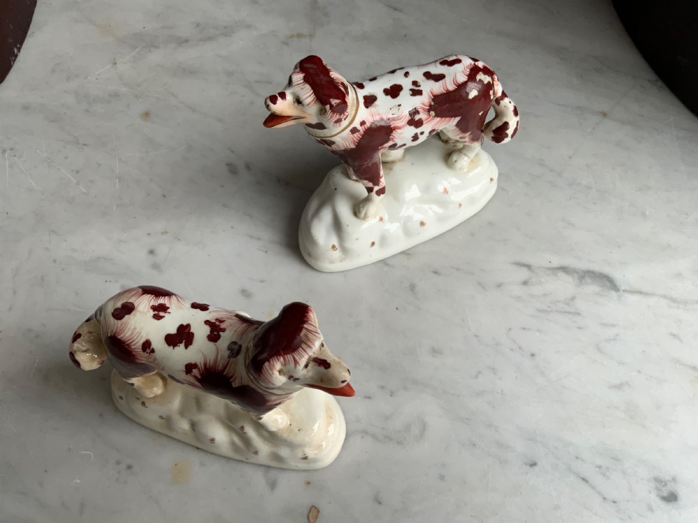 A facing pair of antique ceramic dog figurines decorated with rust-red painted patches on white bases with gilded collars. View VII
