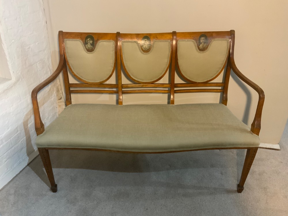 An early 19th-century Regency satinwood chair-back settee featuring three painted portrait medallions and light green fabric upholstery.