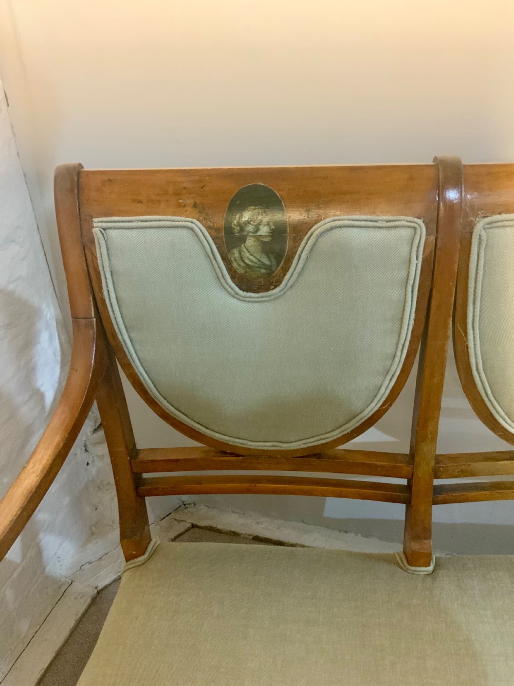 An early 19th-century Regency satinwood chair-back settee featuring three painted portrait medallions and light green fabric upholstery. View II