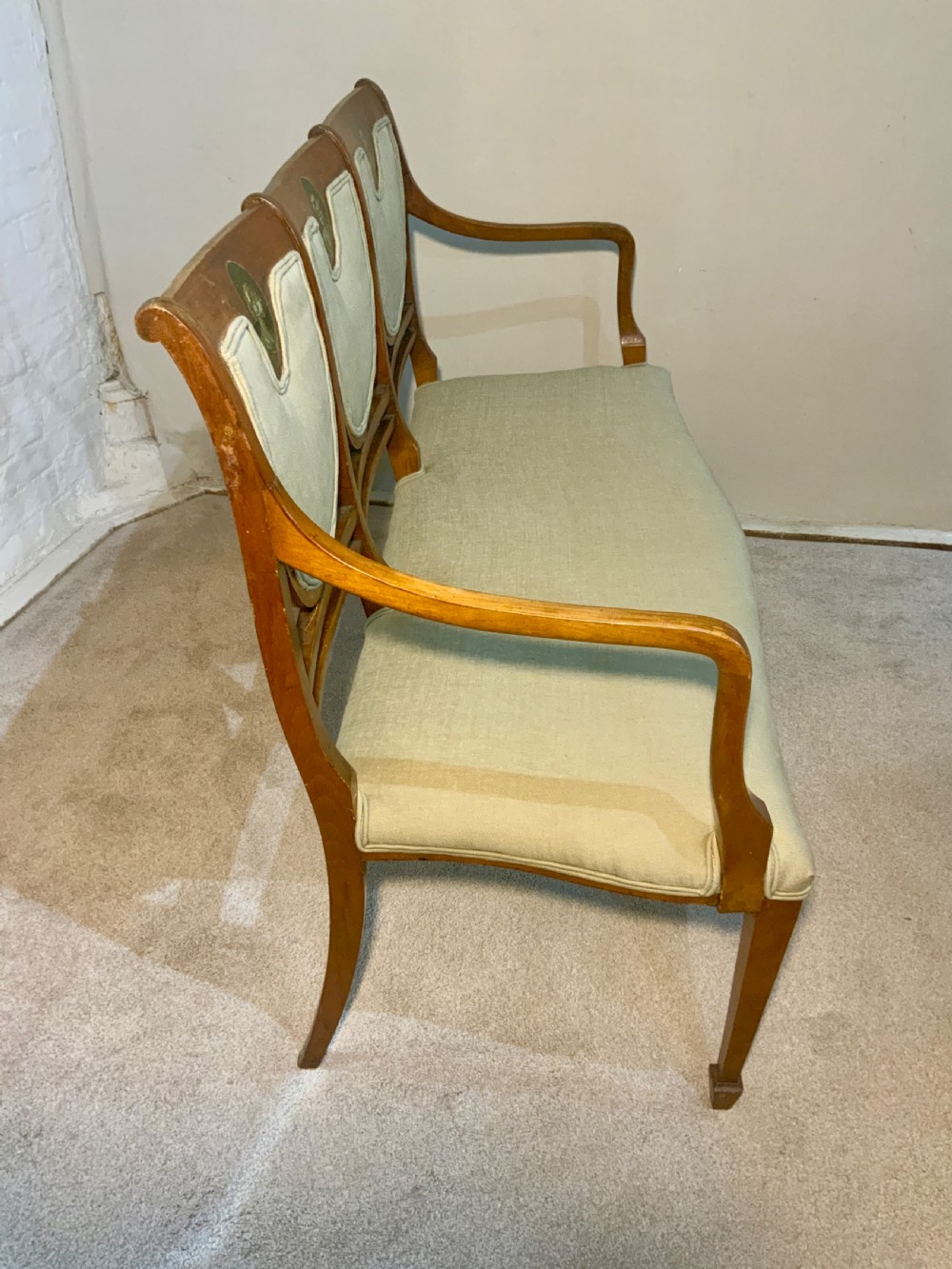 An early 19th-century Regency satinwood chair-back settee featuring three painted portrait medallions and light green fabric upholstery. View V