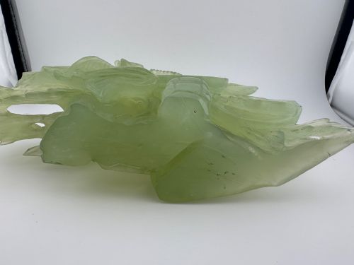 fig 8. A carved pale green Xiuyan jade sculpture depicting a lotus flower, foliage, and a central cash coin, displayed on a dark carved wooden stand.