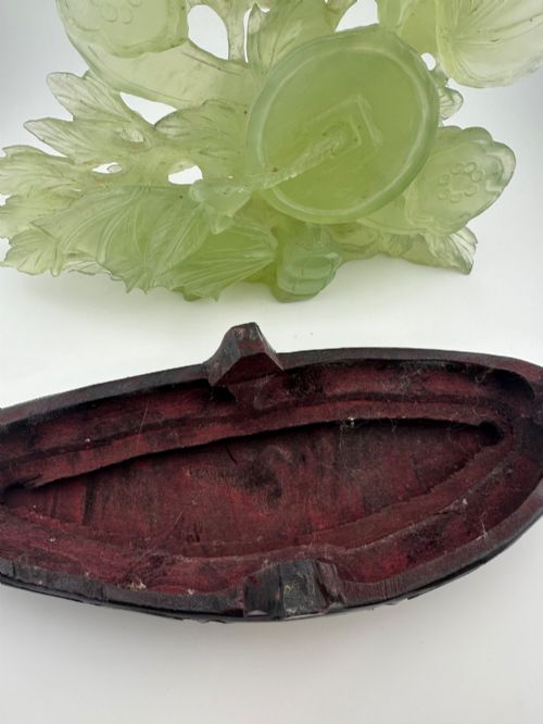 fig 11. A carved pale green Xiuyan jade sculpture depicting a lotus flower, foliage, and a central cash coin, displayed on a dark carved wooden stand.