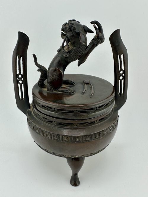 fig 5. A dark patinated bronze tripod censer featuring raised loop handles, a decorative meander border, and a fitted lid with a standing Qilin finial.