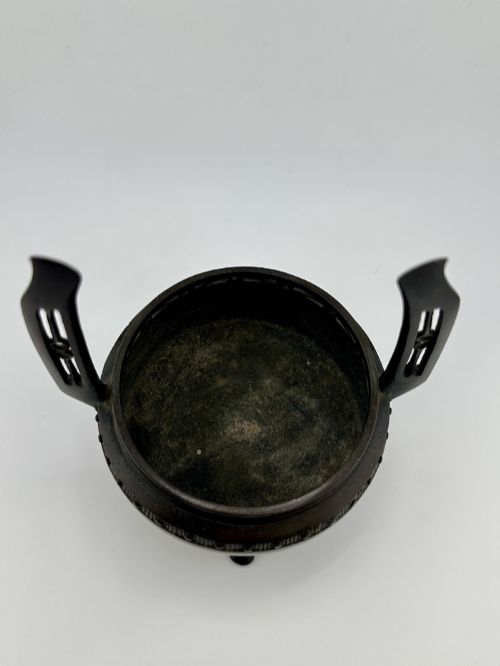 fig 6. A dark patinated bronze tripod censer featuring raised loop handles, a decorative meander border, and a fitted lid with a standing Qilin finial.