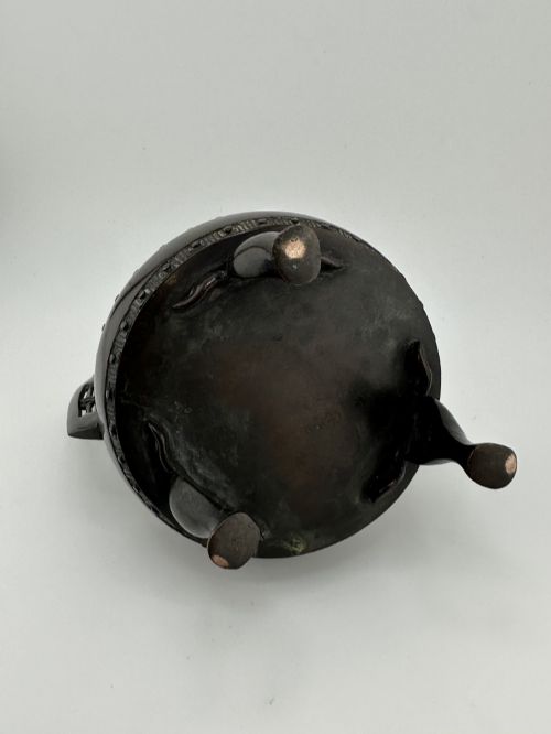 fig 7. A dark patinated bronze tripod censer featuring raised loop handles, a decorative meander border, and a fitted lid with a standing Qilin finial.