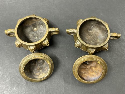 fig 2. A pair of patinated bronze tripod censers featuring sculpted dragon finials on the lids, side handles, and relief mask carvings around the circular bodies.