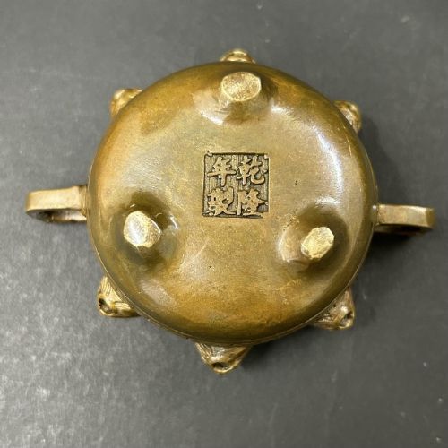 fig 4. A pair of patinated bronze tripod censers featuring sculpted dragon finials on the lids, side handles, and relief mask carvings around the circular bodies.
