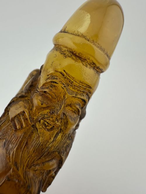 fig 3. A hand-carved honey amber pendant depicting the Chinese deity Shoulao with incised robe detailing and a high domed head.