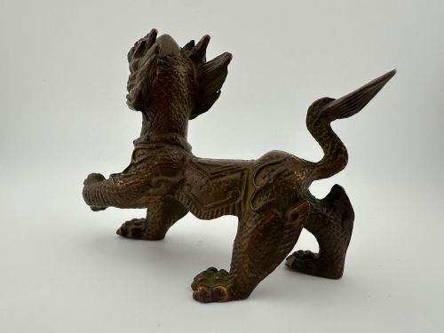 fig 4. A small patinated dark brown bronze figure of a Chinese mythical beast, standing on four legs with an open mouth and raised tail.