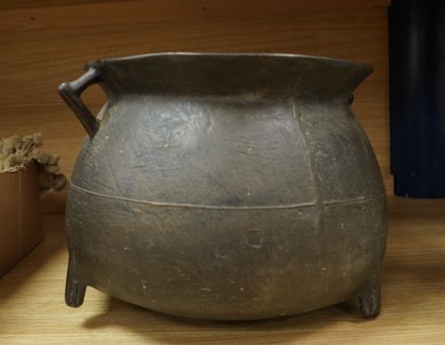 fig 1. A 17th-century leaded bronze cauldron with a bulbous body, three short feet, angular side handles, and a dark patinated surface.