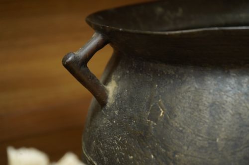 fig 3. A 17th-century leaded bronze cauldron with a bulbous body, three short feet, angular side handles, and a dark patinated surface.