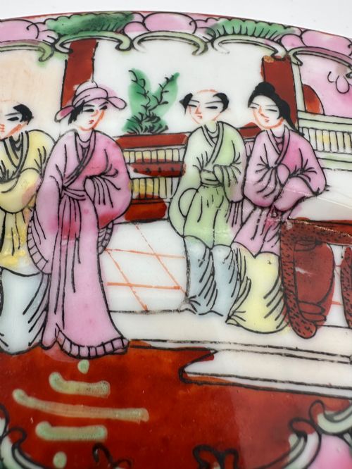 fig 2. A circular hand-painted ceramic charger with alternating panels depicting human figures and floral motifs in green, pink, and red enamels with gold accents.