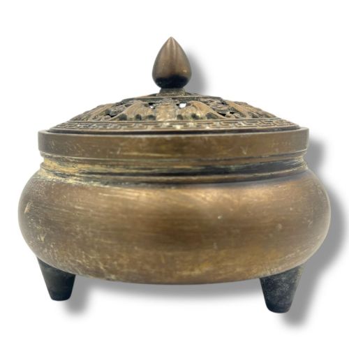 fig 2. A Chinese bronze tripod censer featuring a compressed circular body, three tapered feet, and a reticulated lotus lid topped with a pointed finial.
