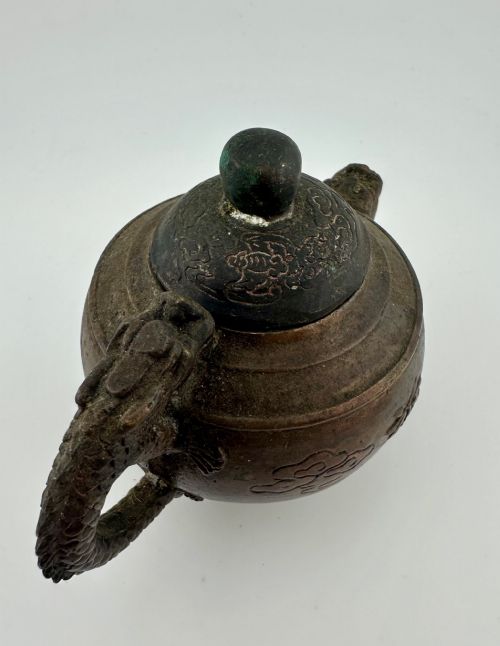 fig 3. A dark cast bronze Chinese teapot featuring a sculpted dragon handle, a dragon-head spout, and raised Chinese character carvings on the main body.