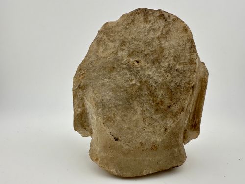 fig 2. A carved off-white hardstone head fragment featuring facial features, elongated earlobes, and faint traces of gilding across the surface.